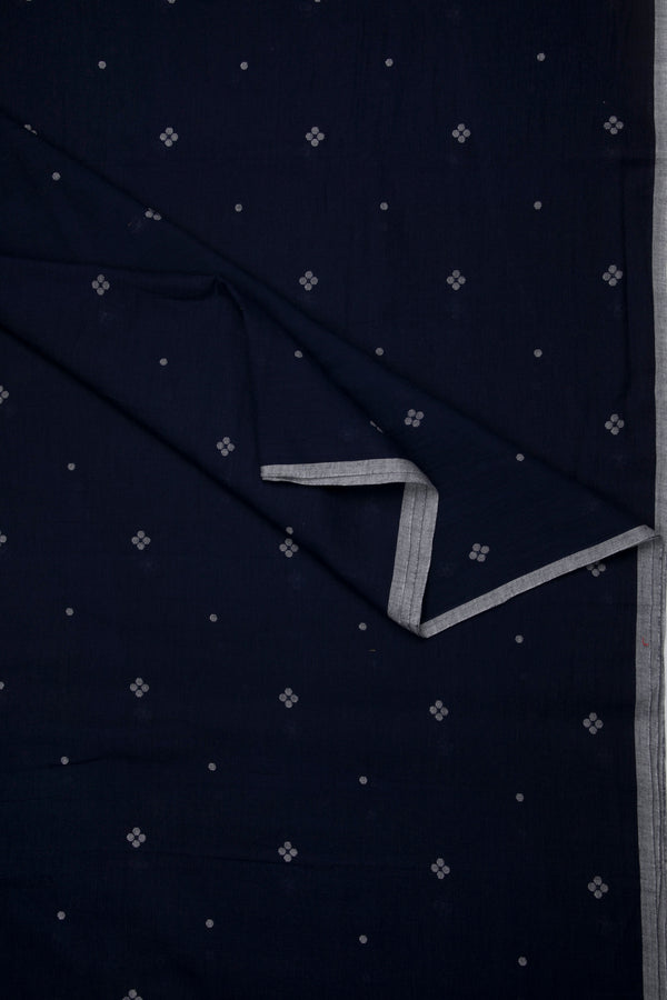 Artisan-made dark indigo Jamdani cotton fabric with delicate floral weaving and grey selvedge edge, sustainable textile from Bengal