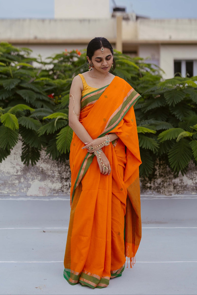 Model wearing Bengal handwoven jamdani saree in orange cotton with zari-striped pallu.