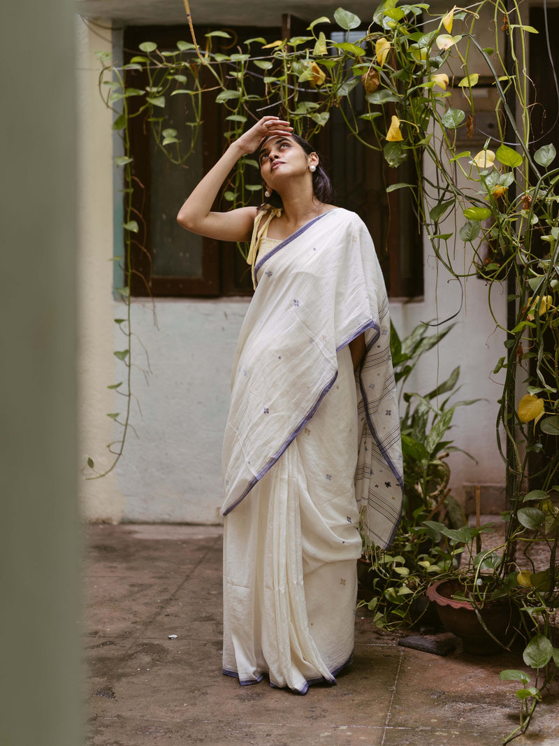 Elegant model in a handwoven indigo-on-white jamdani saree, highlighted by floral pallu details and a stylish yellow bow blouse.