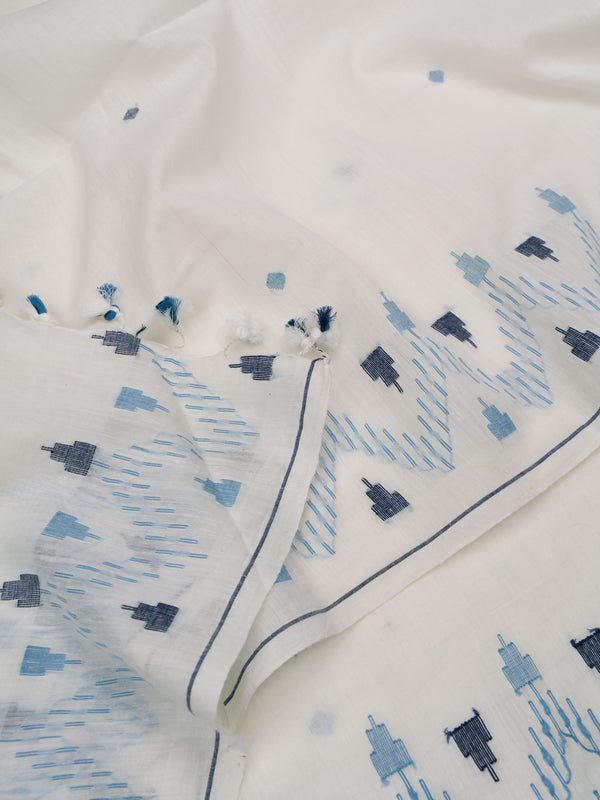 Hand holding the drape of a white and indigo cotton Jamdani saree showing border pattern and tassels by varsaaedit