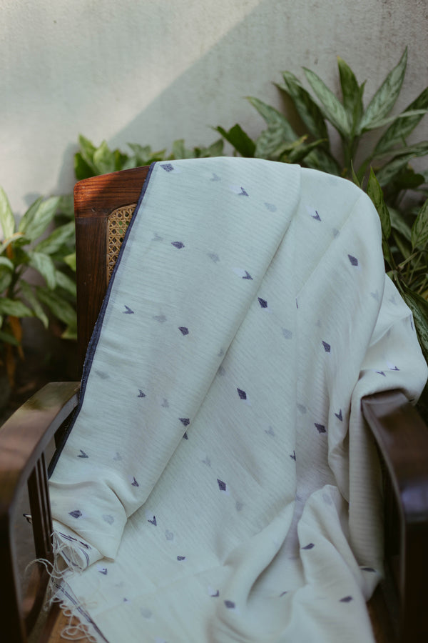 White and Indigo handloom linen Jamdani saree with delicate woven motifs draped on a chair.