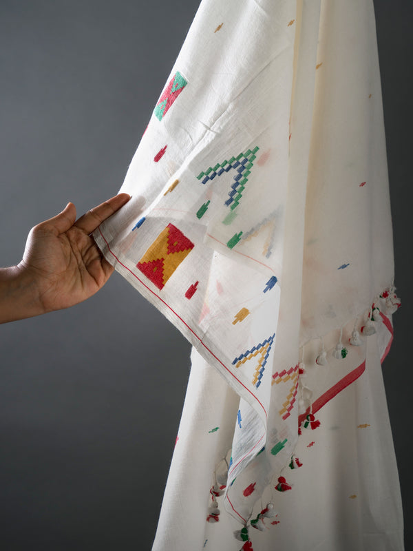 White jamdani saree with colorful geometric patterns held by a hand against a gray background from varsaaedit