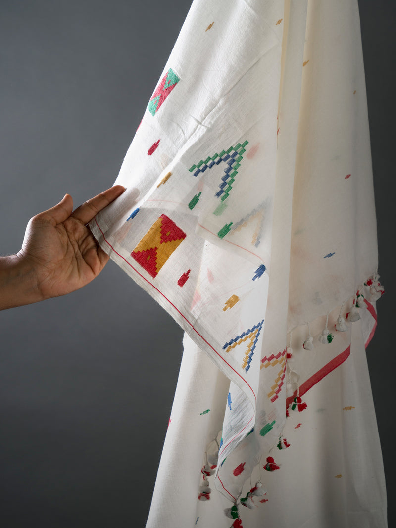 White jamdani saree with colorful geometric patterns held by a hand against a gray background from varsaaedit