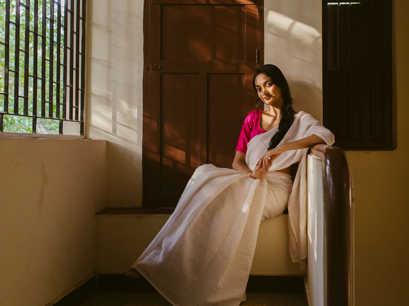 Classic handwoven muslin saree with golden stripes and pink blouse, perfect for festive occasions
